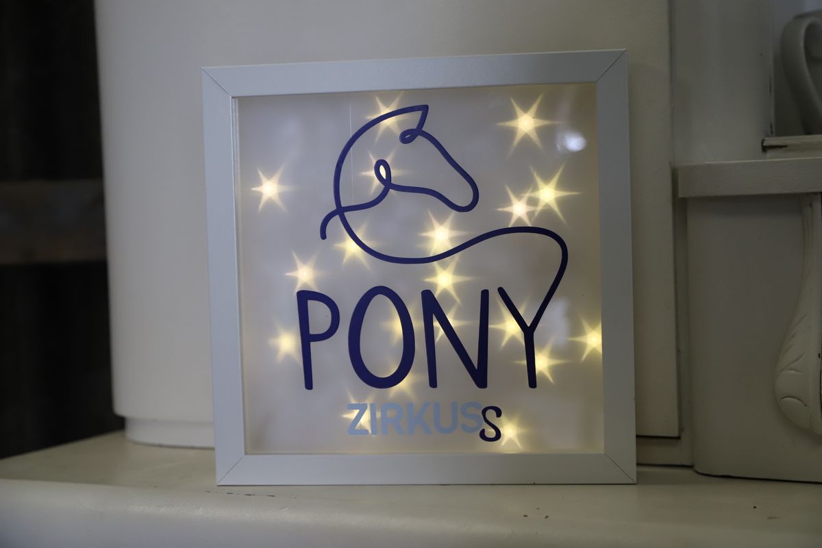 Beleuchtetes Ponyzirkuss-Logo in einem Rahmen mit warmen Lichtpunkten