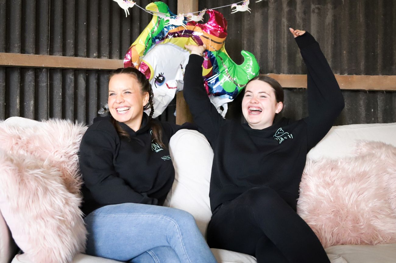 Nena und Lilith sitzen lachend auf einem Sofa in der Scheune, darüber ein Einhornballon